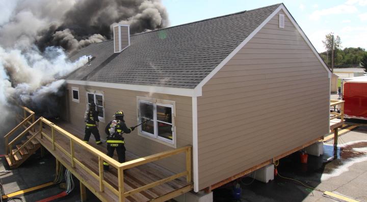 house on fire with firefighters opening windows