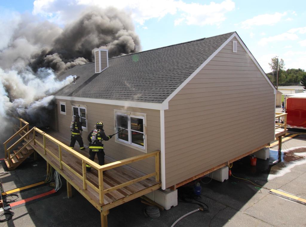 house on fire with firefighters opening windows