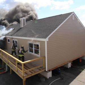 house on fire with firefighters opening windows