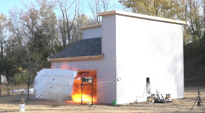 Garage door is blown off of test structure following explosion as a result of thermal runaway test.