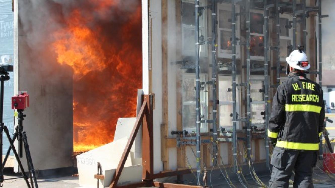 A target facade is exposed to a post-flashover fire from a source compartment to study structure-to-structure fire spread.